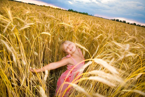 Klein meisje springt in een tarweveld. tegen de achtergrond van bewolkt s — Stockfoto