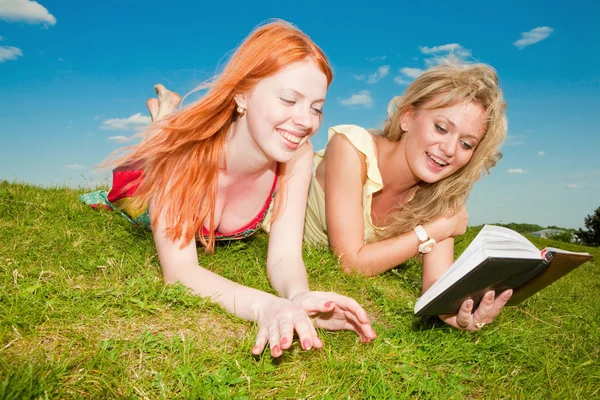 两个漂亮的女孩与户外的笔记本 躺在绿草地上 免版税图库照片