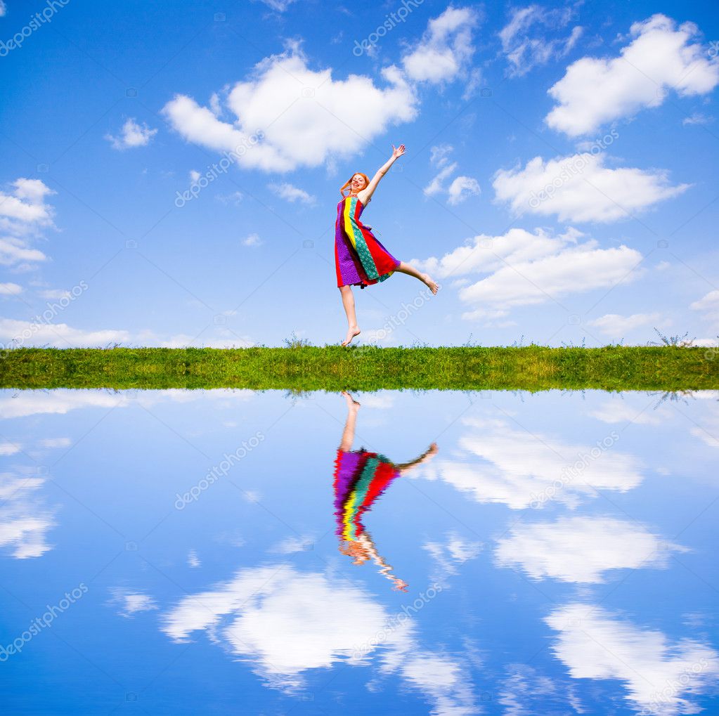 Happy girl jumping together on green meadow. Reflected in water