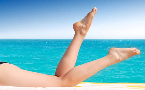 Sexy weibliche Beine gegen türkisfarbenes Meer — Stockfoto
