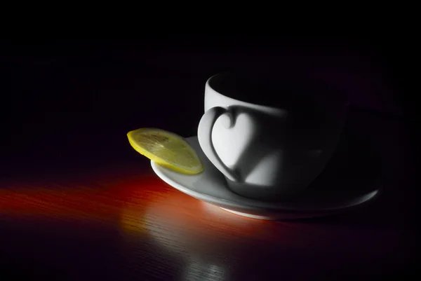 White on saucer cup with lemon in dark — Stock Photo, Image