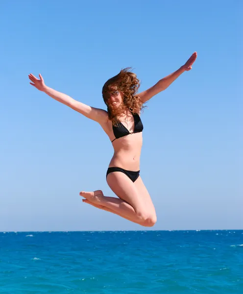 Young beautiful woman jumps against the sea — Stock Photo, Image