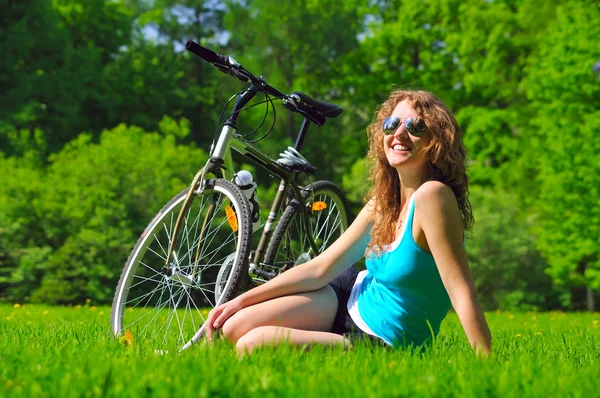 Zittende vrouw in de buurt van haar fiets in park — Stockfoto