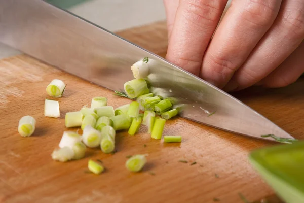Handen van cook snijden lente-uitjes — Stockfoto