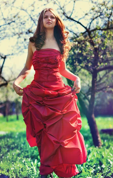 Jonge vrouw in rode jurk in tuin — Stockfoto