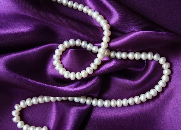 Pérolas brancas em uma seda lilás — Fotografia de Stock