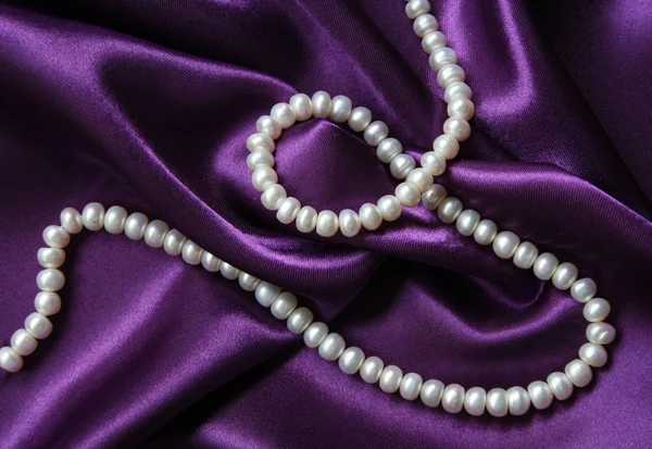 Pérolas brancas em uma seda lilás — Fotografia de Stock