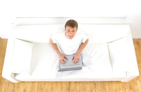 Πορτρέτο ενός νεαρού άνδρα, χαλαρωτικό στον καναπέ, ενώ χρησιμοποιώντας ένα φορητό υπολογιστή — Φωτογραφία Αρχείου
