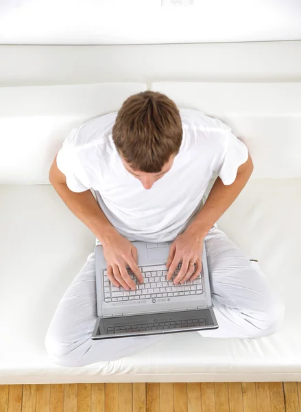 Portrait of a young man relaxing on couch while using a laptop — Stock Photo, Image