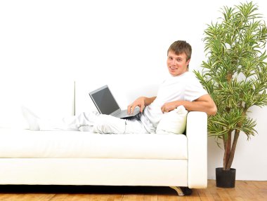 Smiling young man working on laptop computer at home clipart