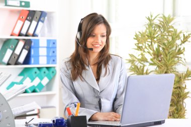 Portrait of a beautiful business woman working at her desk with a headset a clipart