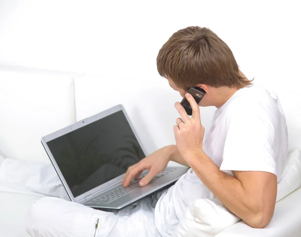 Cep telefonu ile bir dizüstü bilgisayar üzerinde konuşan genç bir adam portresi — Stok fotoğraf