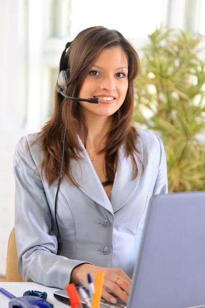 Vacker affärskvinna arbetar på hennes skrivbord med ett headset och laptop — Stockfoto