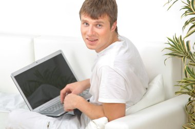 Smiling young man working on laptop computer at home clipart