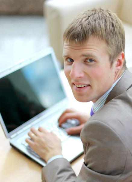 Бизнесмен сидит за столом в офисе, работает с ноутбуком, смотрит — стоковое фото
