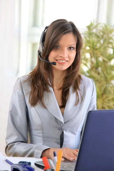 Mooie zakenvrouw werken bij haar bureau met een headset en laptop — Stockfoto