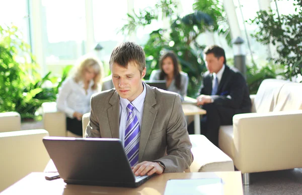 Junge Führungskraft arbeitet am Laptop mit Kollegen im Hintergrund — Stockfoto