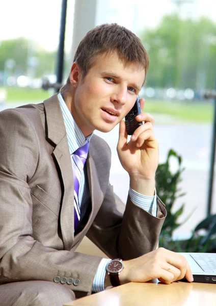 Empresario sentado en la mesa en el pasillo de la oficina, hablando por teléfono móvil y nosotros — Foto de Stock