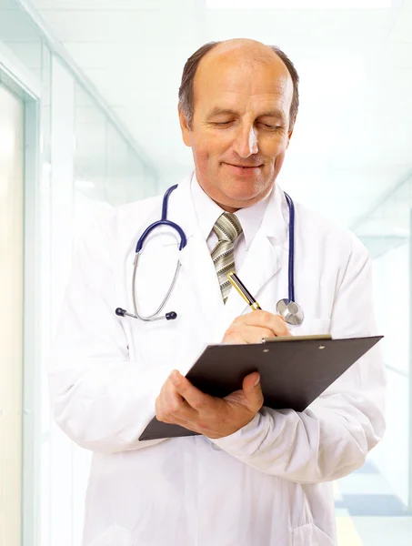 Happy smiling mature doctor writing on clipboard in a modern hospital Royalty Free Stock Images