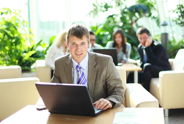 Jonge uitvoerende werken op een laptop met collega's op de achtergrond — Stockfoto