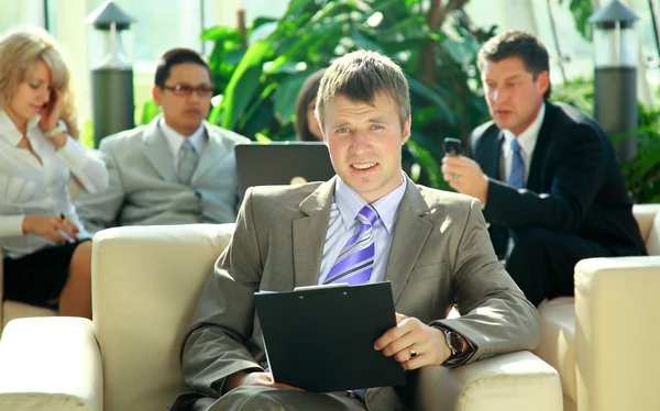 Retrato de um jovem homem de negócios feliz com colegas em segundo plano — Fotografia de Stock