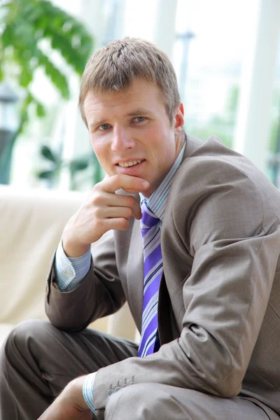 Portrait of a smiling handsome young businessman sitting on chair in office — Stock Photo, Image