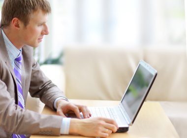 Businessman sitting at desk in office, working with laptop computer, lookin clipart