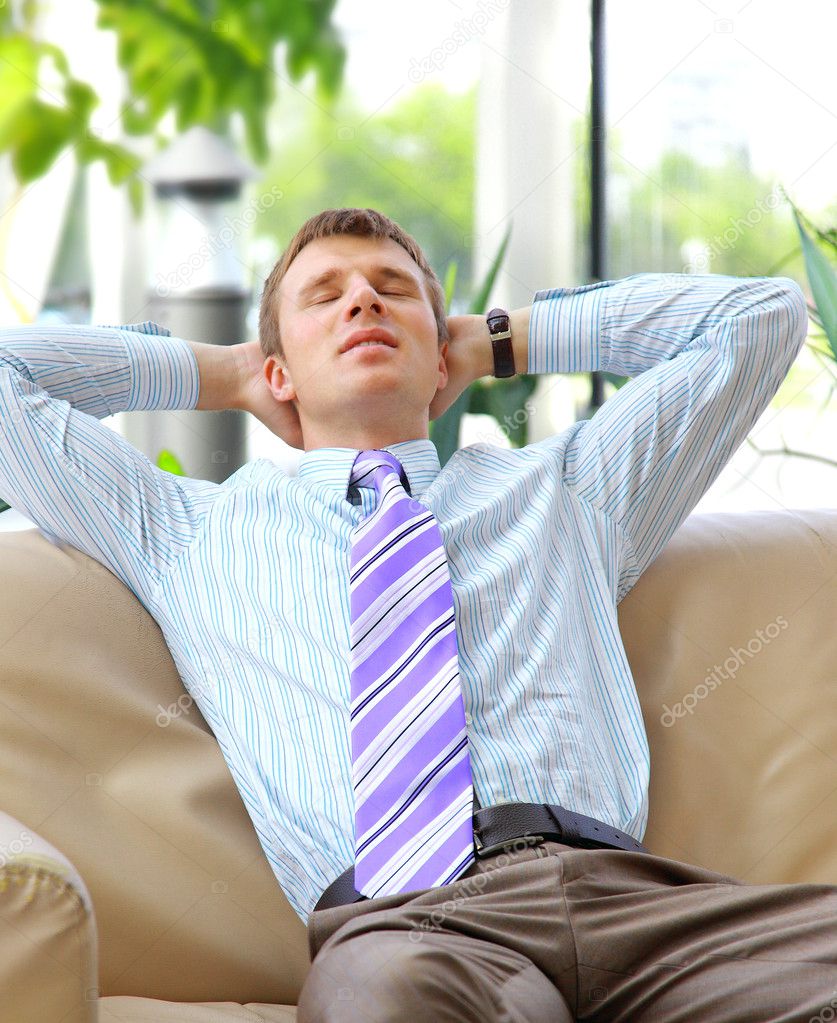 Young relaxed business man with hands behind head at work