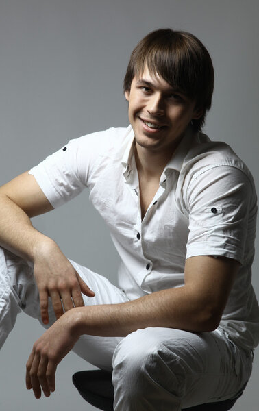 Portrait of a casual young satisfied man sitting relaxed. Isolated on white.