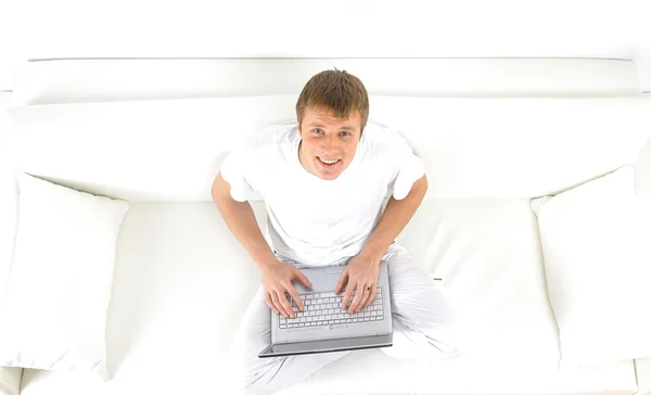 Πορτρέτο ενός νεαρού άνδρα, χαλαρωτικό στον καναπέ, ενώ χρησιμοποιώντας ένα φορητό υπολογιστή — Φωτογραφία Αρχείου