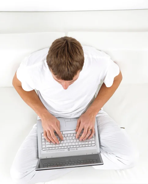 一个年轻人休闲沙发同时使用一台笔记本电脑上的肖像 — 图库照片