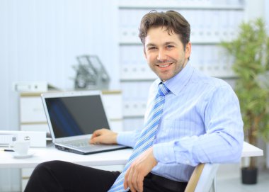 Businessman sitting at office desk working on laptop computer clipart