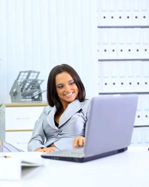 在办公室、 便携式计算机上工作的年轻女商人微笑 — 图库照片