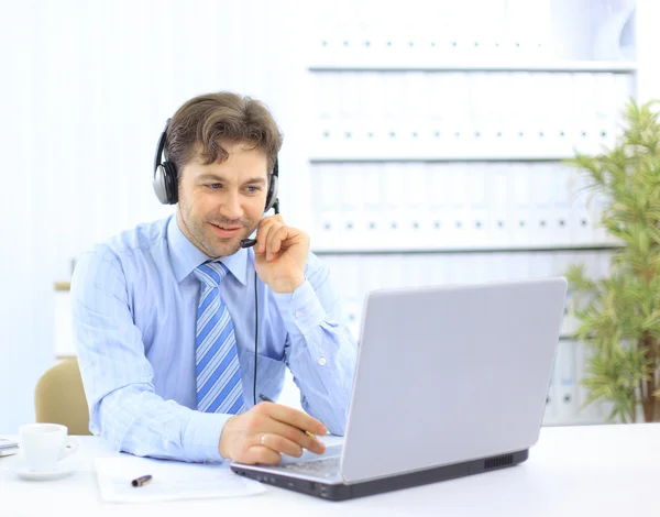 Närbild av en affärsman med headset. Han arbetar på laptop — Stockfoto