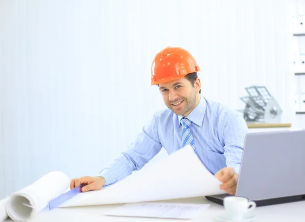 Arquiteto olhando para trabalhar no escritório na mesa. Vestindo hardhat e tomando não — Fotografia de Stock