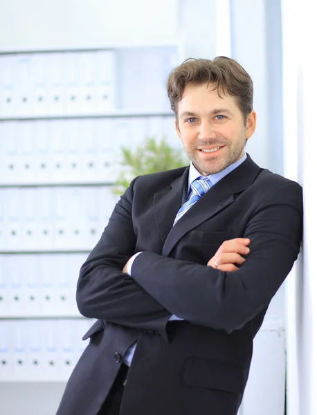 Νέος επιχειρηματίας στέκεται στο λόμπι του γραφείο, χρησιμοποιώντας smartphone, χαμογελώντας — Φωτογραφία Αρχείου
