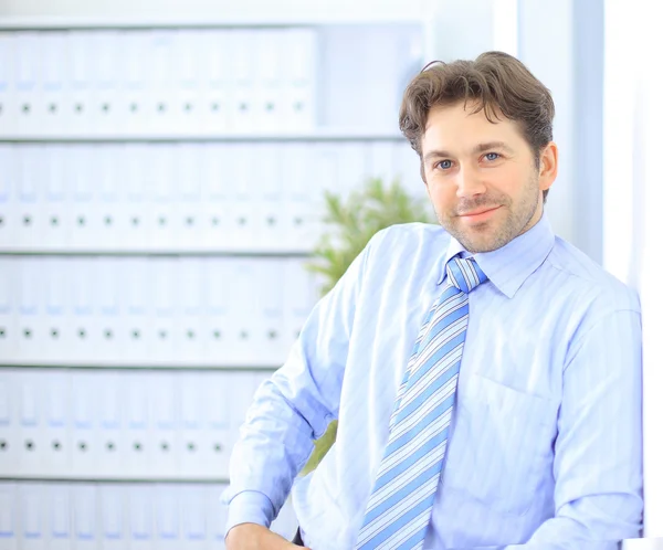 Νέος επιχειρηματίας στέκεται στο λόμπι του γραφείο, χρησιμοποιώντας smartphone, χαμογελώντας — Φωτογραφία Αρχείου