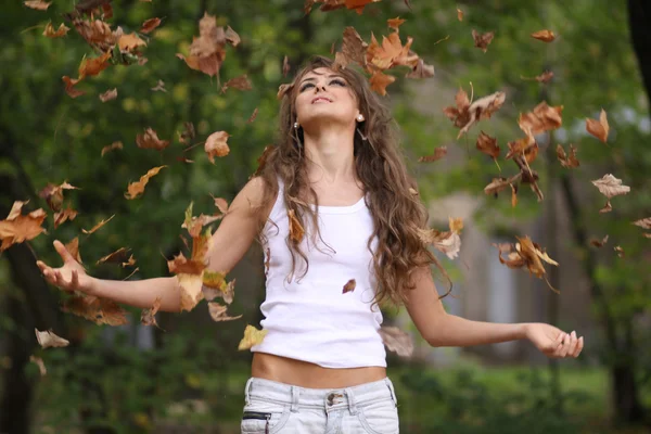 Счастливая девушка бросает осенние листья — стоковое фото