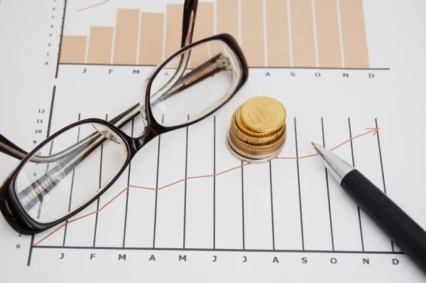 Gráfico de stock, monedas, bolígrafo y gafas — Foto de Stock