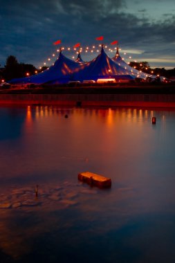 Circus style tent with lights reflected in river clipart