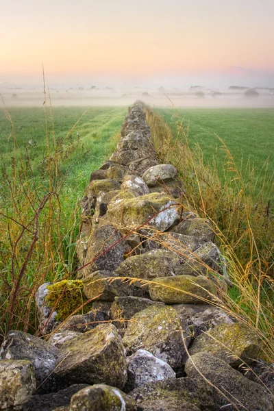 Lever de soleil au champ et mur de pierre disparaissant dans le brouillard, HDR — Photo