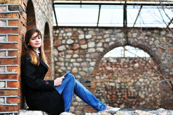 Девушка читает возле кирпичной стены — стоковое фото