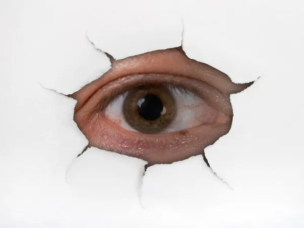 Eye looking through hole on paper — Stock Photo, Image