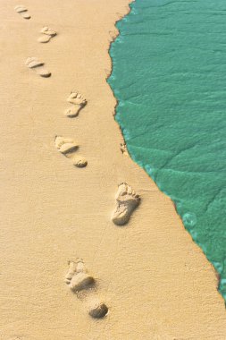 Foot steps and surf on tropical beach clipart