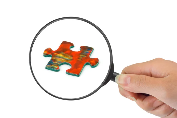 Hand with magnifying glass and puzzle — Stock Photo, Image
