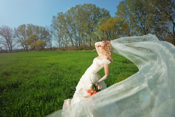 Beautiful bride posing on fresh green grass in sunlight
