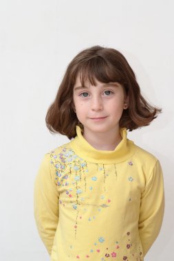 Serious cute little girl stands against the wall clipart