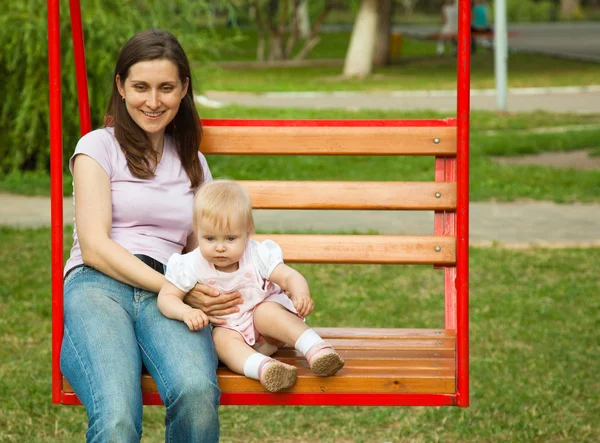 Mãe e uma criança balançando em um playground — Fotografia de Stock