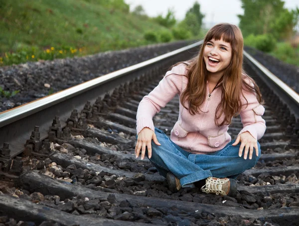 Genç güzel gülen kız demiryolu üzerinde oturur — Stok fotoğraf