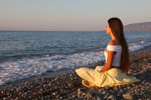 Una mujer está sentada en una playa — Foto de Stock